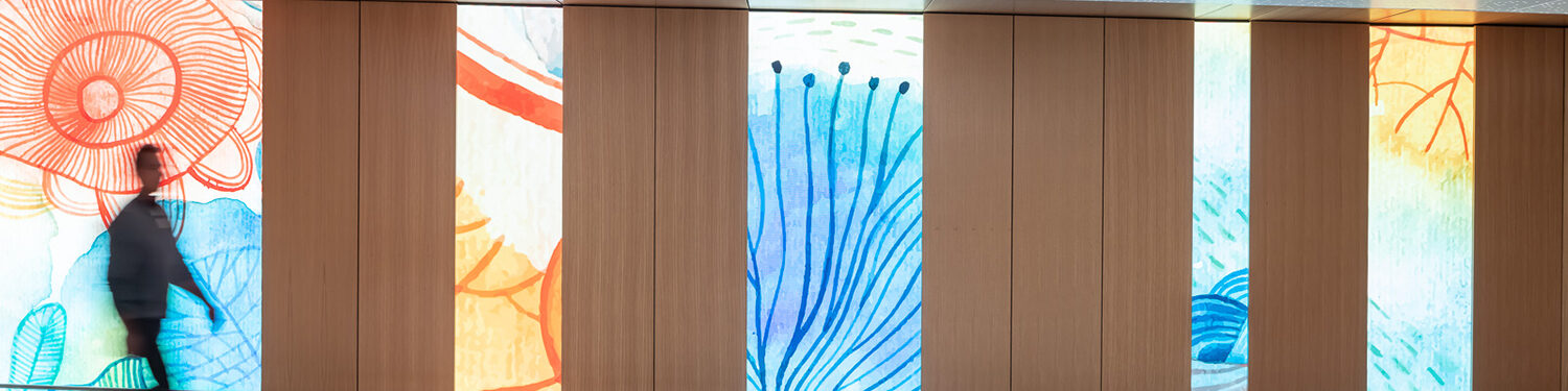 A person uses one of the Mayo Clinic subway pedestrian ramps. The ramp has a slight elevation and is framed by changing video boards with artistic graphics of nature