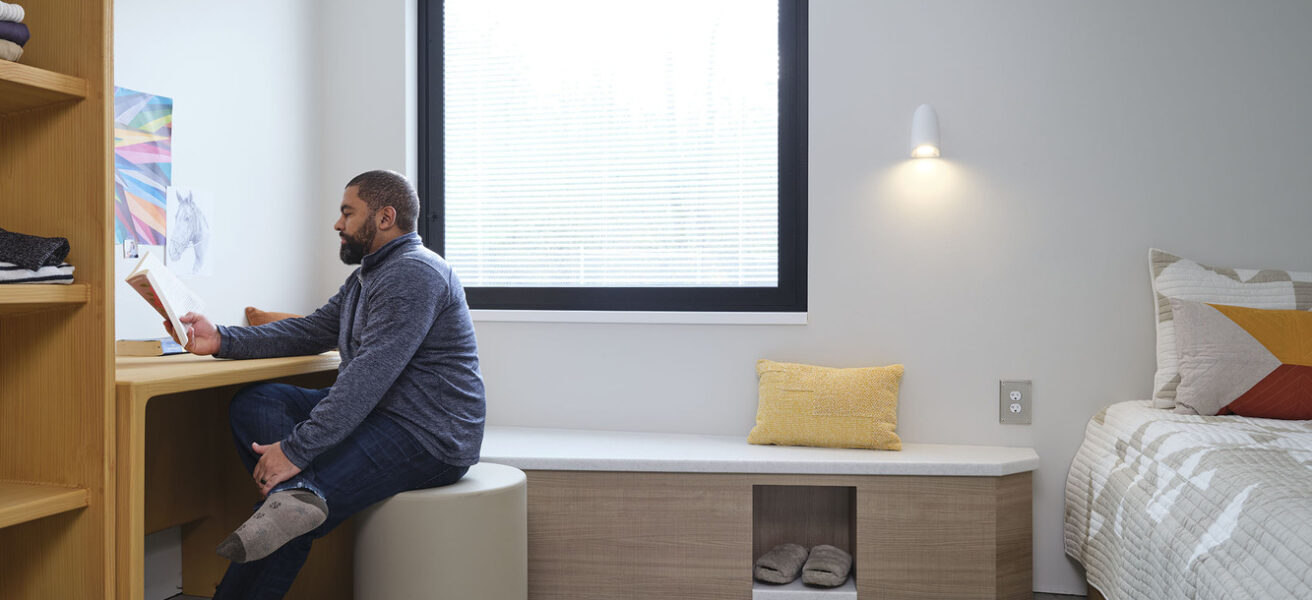 A person sits at the desk in one of the Maple Lane patient bedrooms.